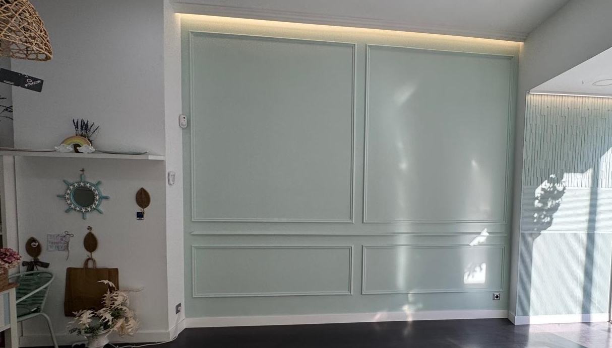 Pared panelada pintada en verde salvia con luz cálida oculta en la cornisa