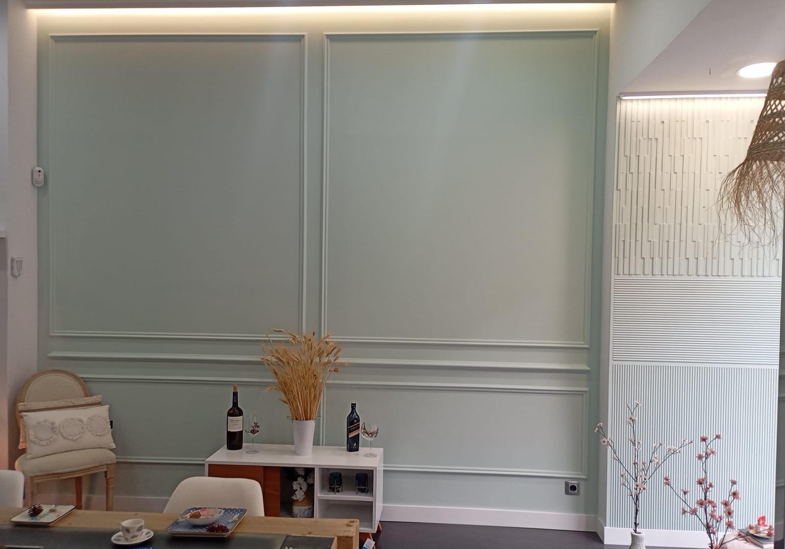 Pared de salón panelada en verde salvia con moldura perimetral y zócalo